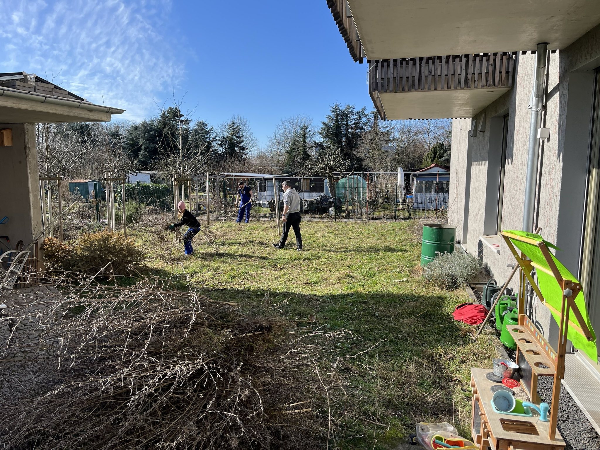 Menschen arbeiten im Garten. Davor ein großer Berg Grünschnitt.